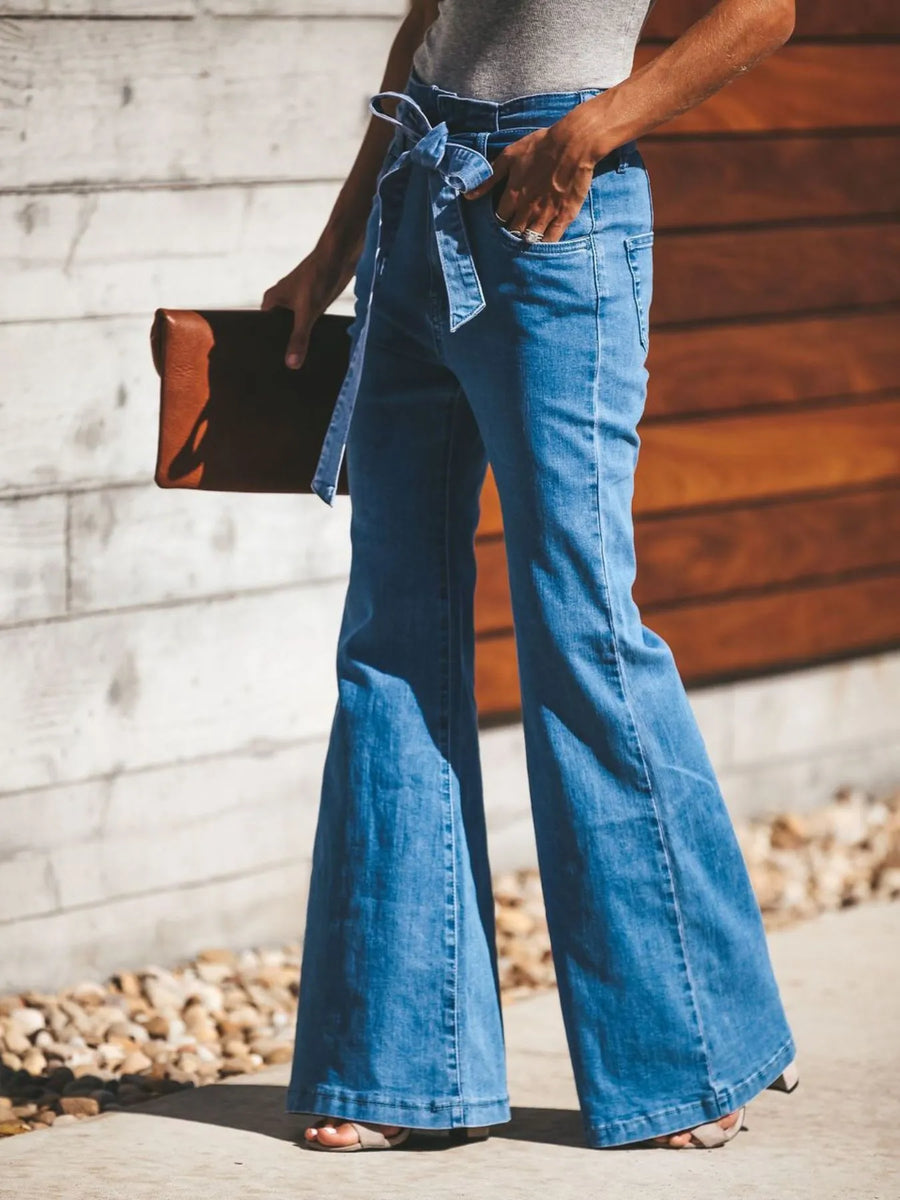 Person wearing blue flared jeans with a wooden background