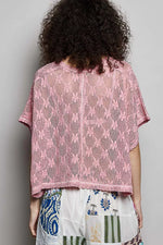 Person wearing a pink lace top with a plain background
