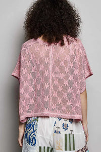 Person wearing a pink lace top with a plain background