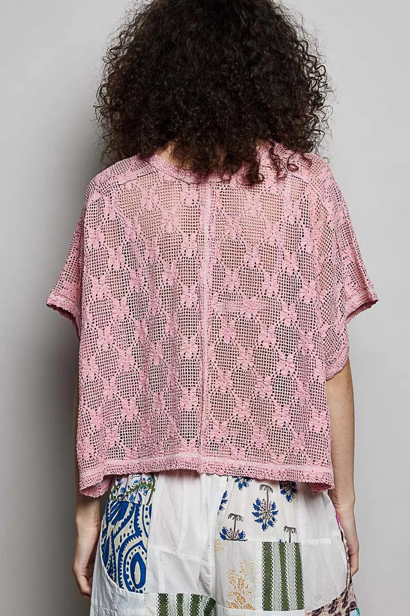 Person wearing a pink lace top with a plain background