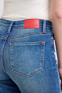 Close-up of blue jeans with a red label on the back pocket, against a neutral background.