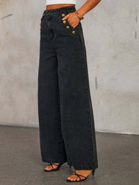 Person wearing wide-leg black jeans with gold buttons against a plain background