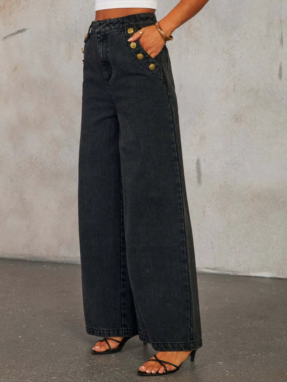 Person wearing wide-leg black jeans with gold buttons against a plain background