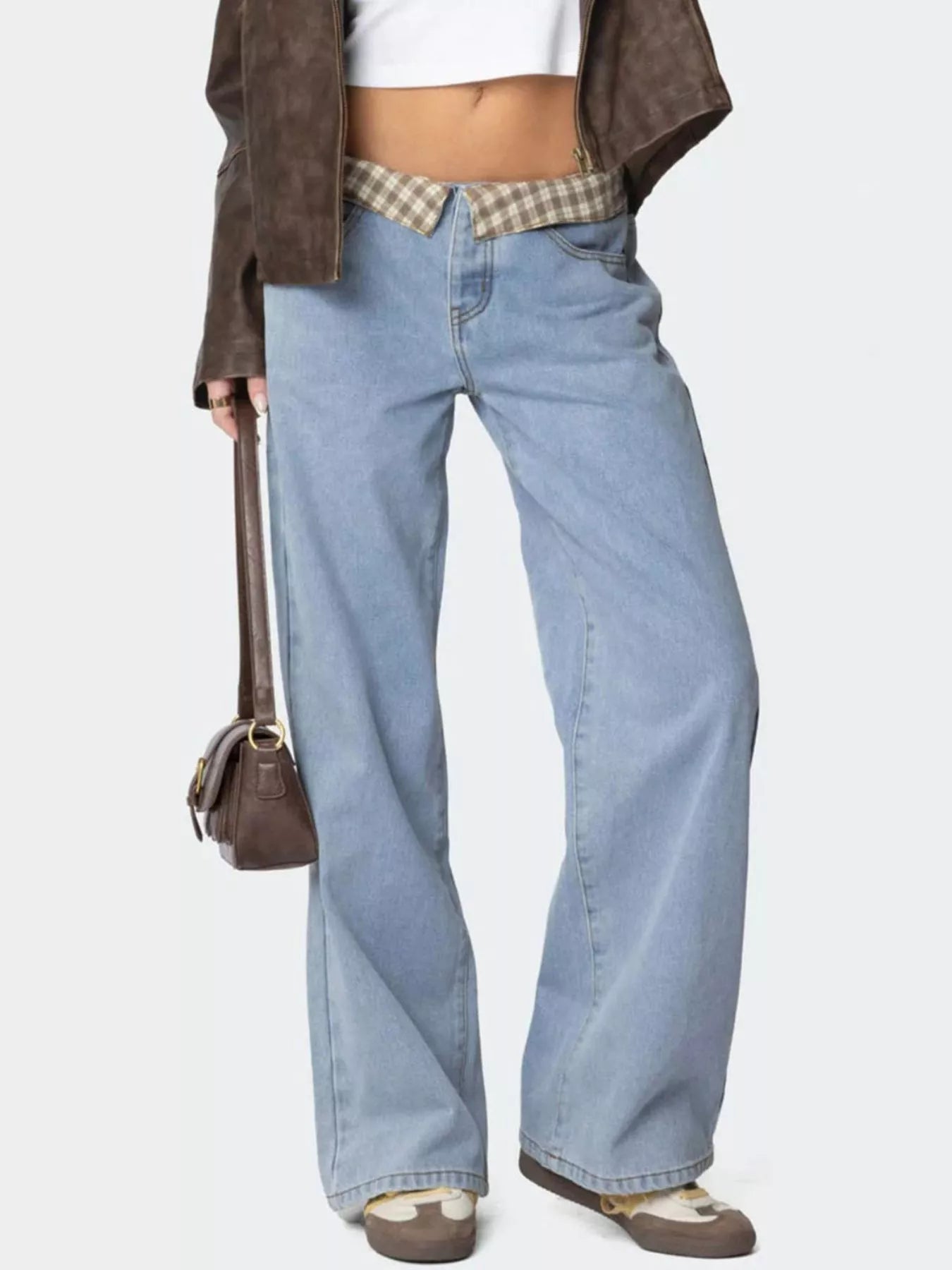 Person wearing light blue flared jeans with a brown jacket and plaid shirt on a white background
