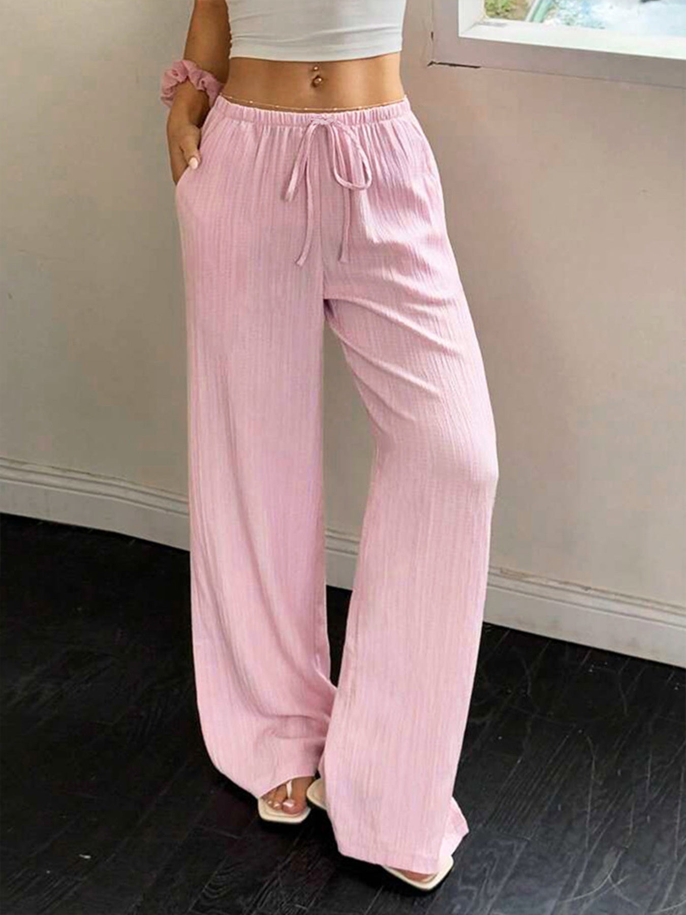 Person wearing light pink wide-leg pants and a white top against a neutral background