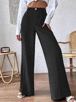 Person wearing black wide-leg pants and a white shirt in a room with a textured wall and wooden floor.