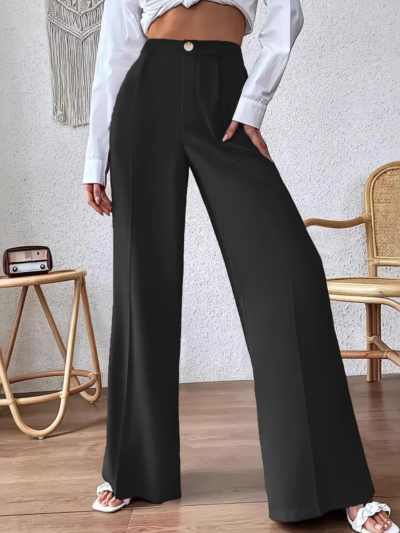 Person wearing black wide-leg pants and a white shirt in a room with a textured wall and wooden floor.