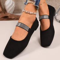 Black flat shoes with decorative straps worn by a person on a neutral background