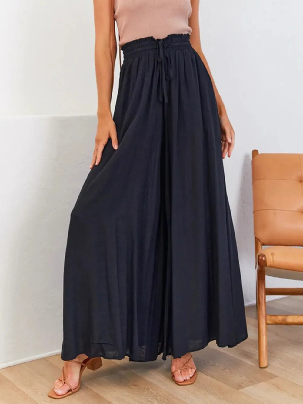 Person wearing a long navy skirt with a beige top and sandals in a minimal indoor setting.