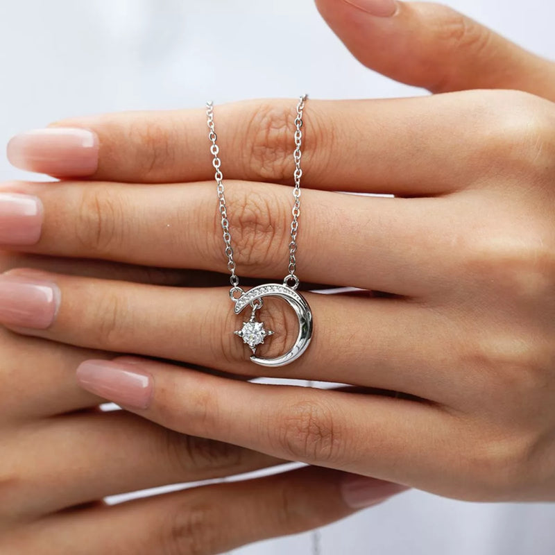 Silver necklace with a moon and star pendant held between fingers on a white background