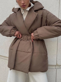 Person wearing a brown puffer coat against a light stone wall.