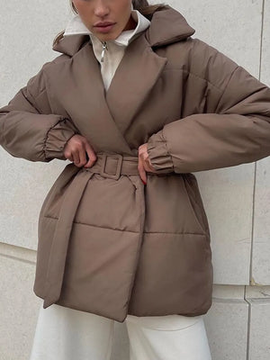 Person wearing a brown puffer coat against a light stone wall.