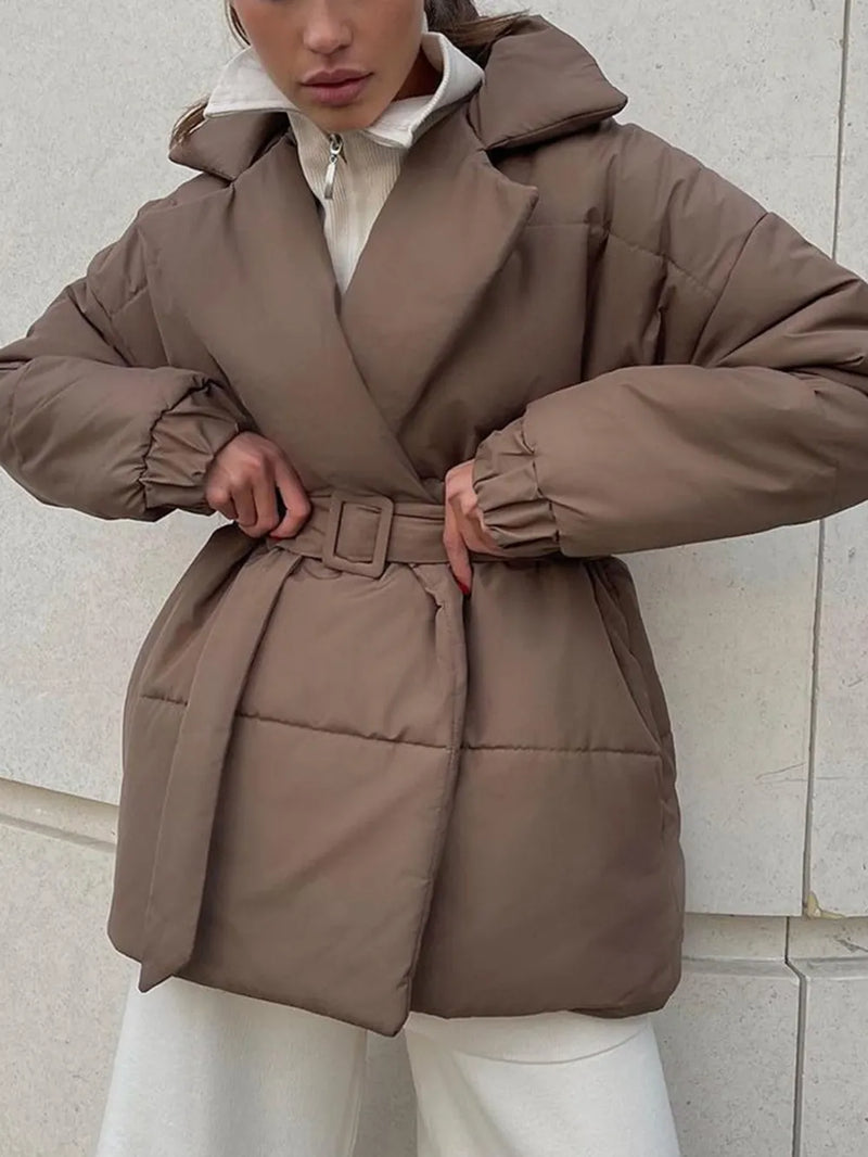 Person wearing a brown puffer coat against a light stone wall.