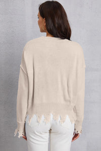 Woman wearing a beige sweater with distressed hem against a gray background