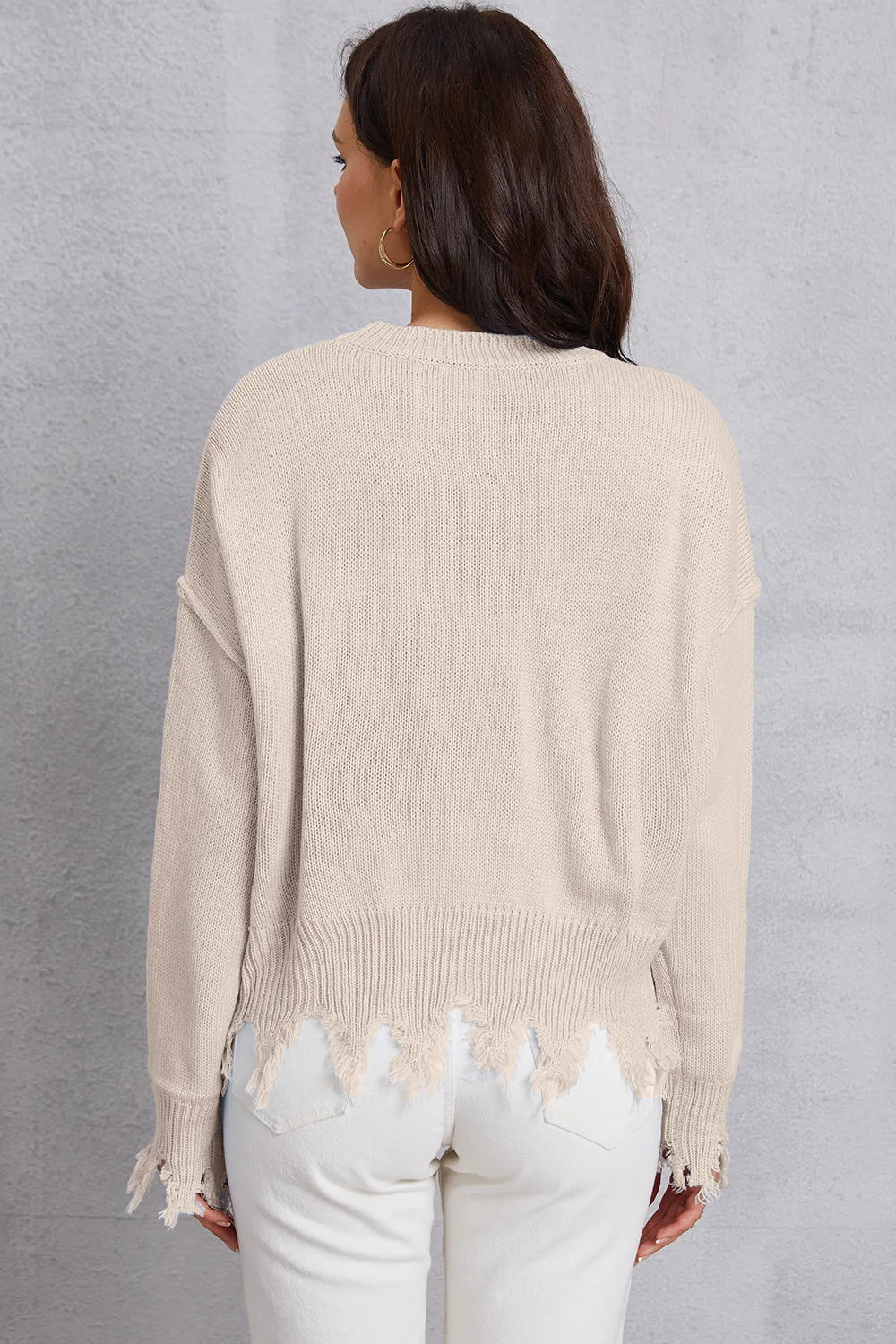 Woman wearing a beige sweater with distressed hem against a gray background