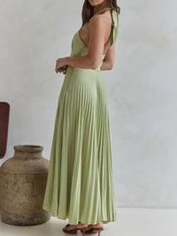 Woman wearing a light green dress standing next to a textured vase against a plain background