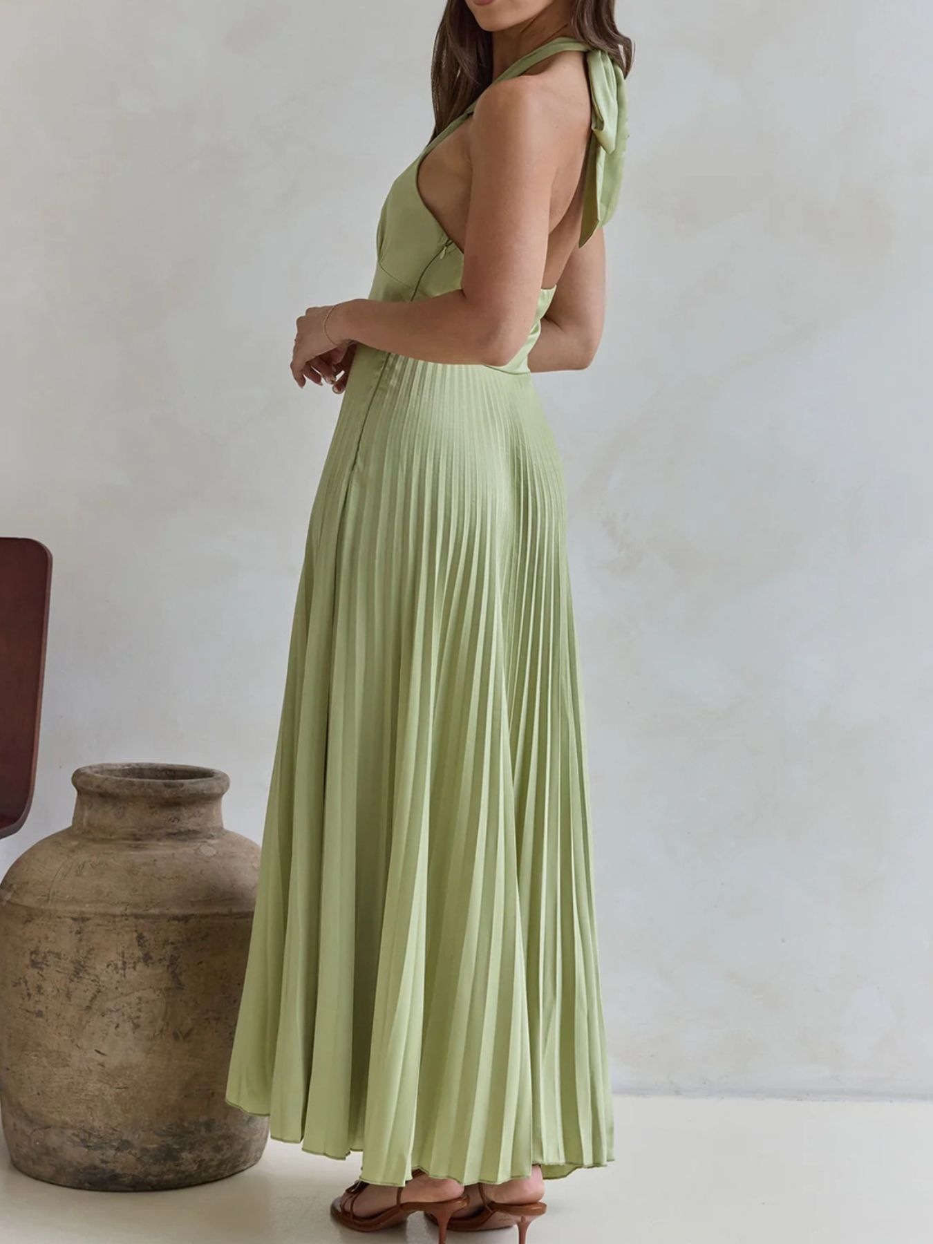 Woman wearing a light green dress standing next to a textured vase against a plain background