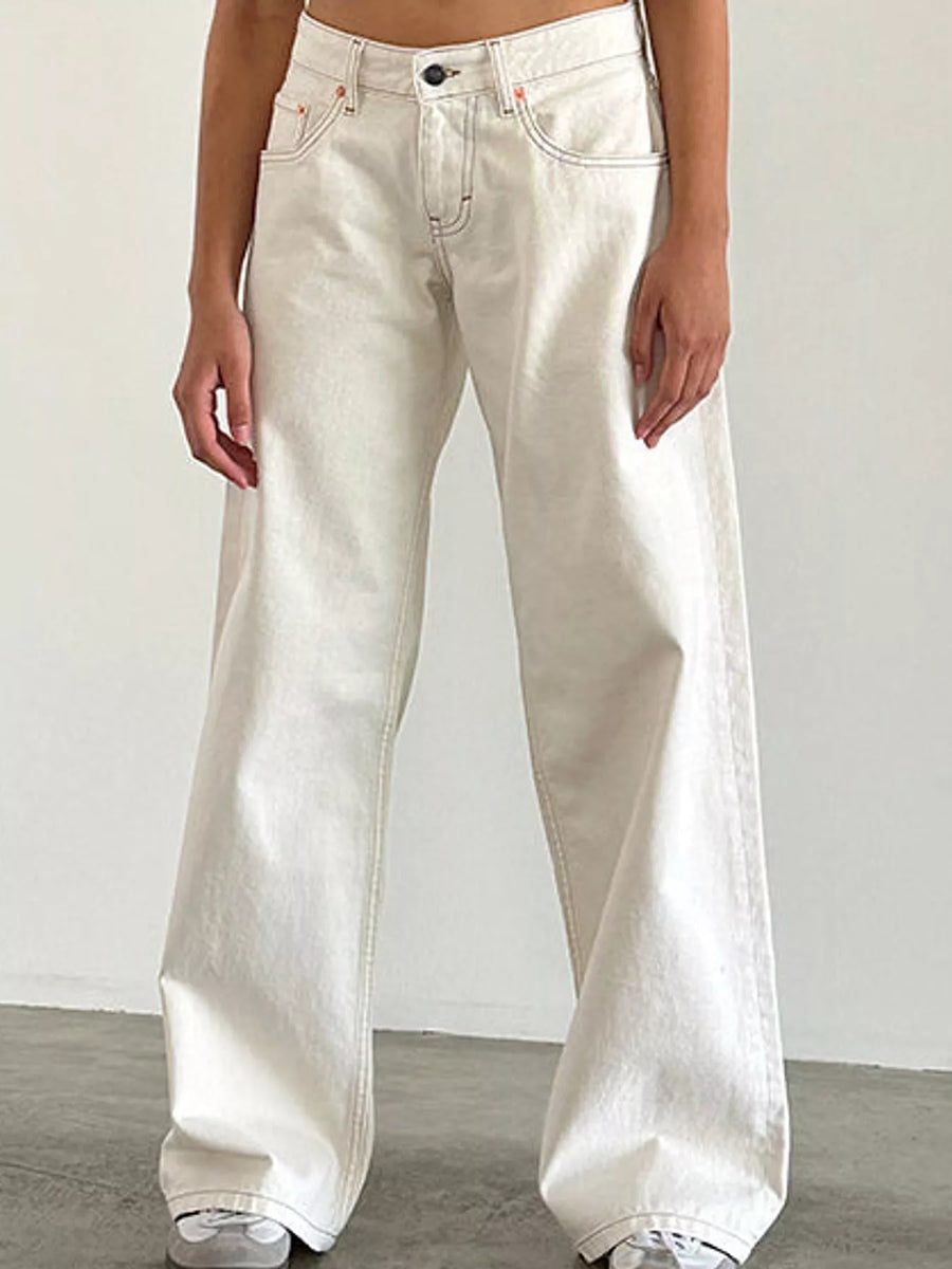 A person wearing off-white wide-leg denim jeans with a relaxed, baggy fit, shown from the waist down against a plain light gray wall and concrete floor.