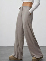 Person wearing beige wide-leg pants with a white top on a plain background
