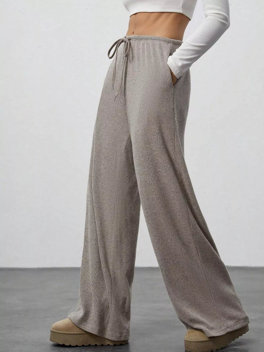 Person wearing beige wide-leg pants with a white top on a plain background