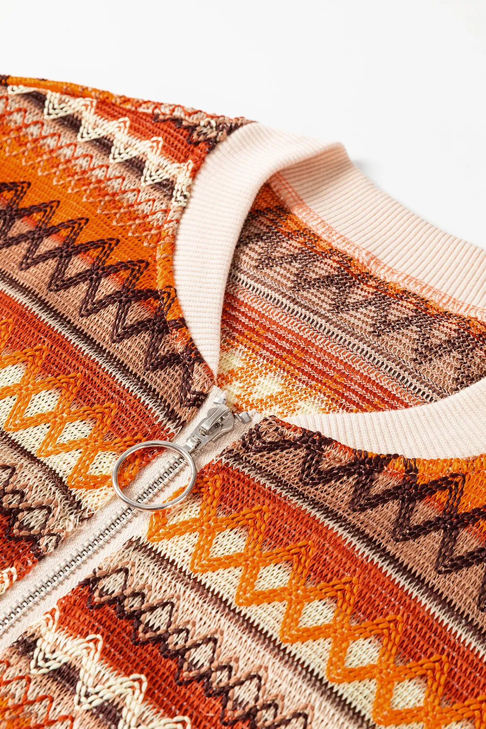 Close-up of a patterned garment with a zipper, featuring orange, brown, and beige colors.