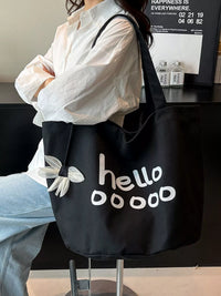 Person holding a black tote bag with 'hello doooo' text and white butterfly design.