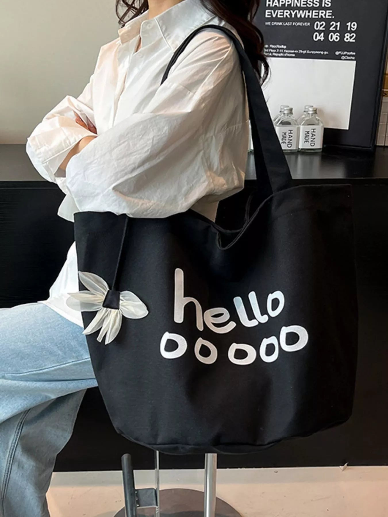 Person holding a black tote bag with 'hello doooo' text and white butterfly design.