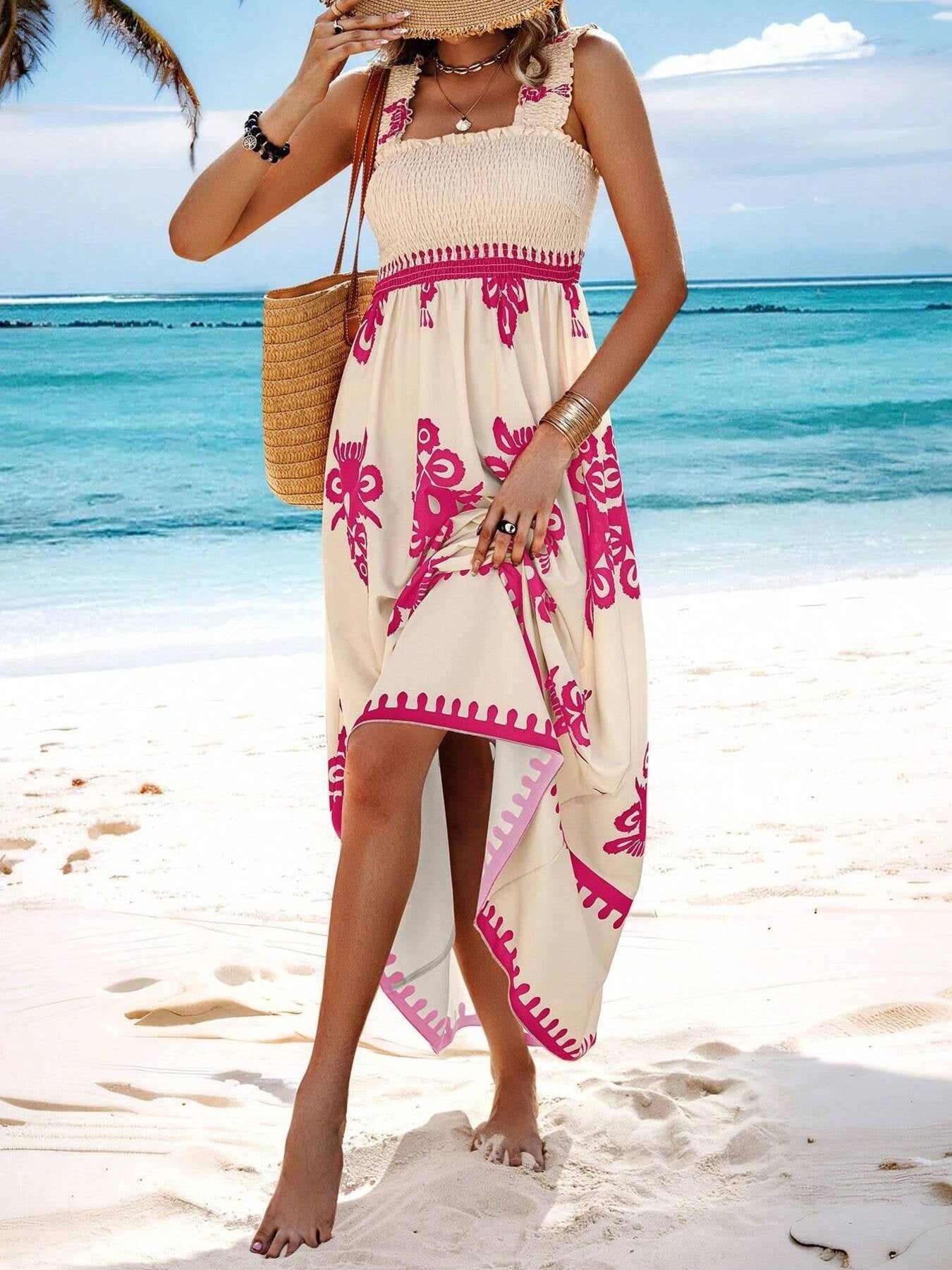 Woman in a beach dress with pink patterns standing on a sandy beach with ocean in the background.