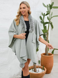 Woman wearing a light gray poncho with fur trim standing next to potted plants.