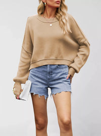 Woman wearing a beige sweater and denim shorts against a plain background