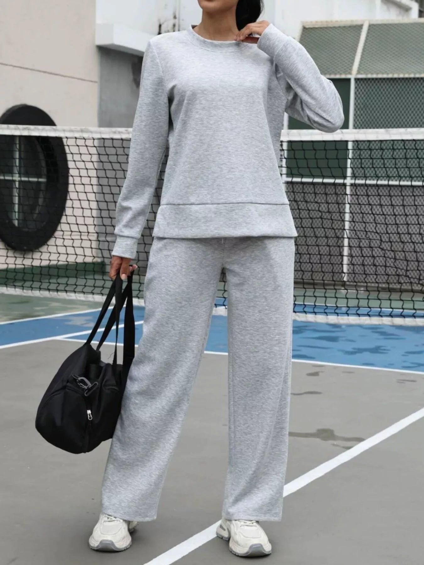 Person wearing a gray tracksuit on a tennis court