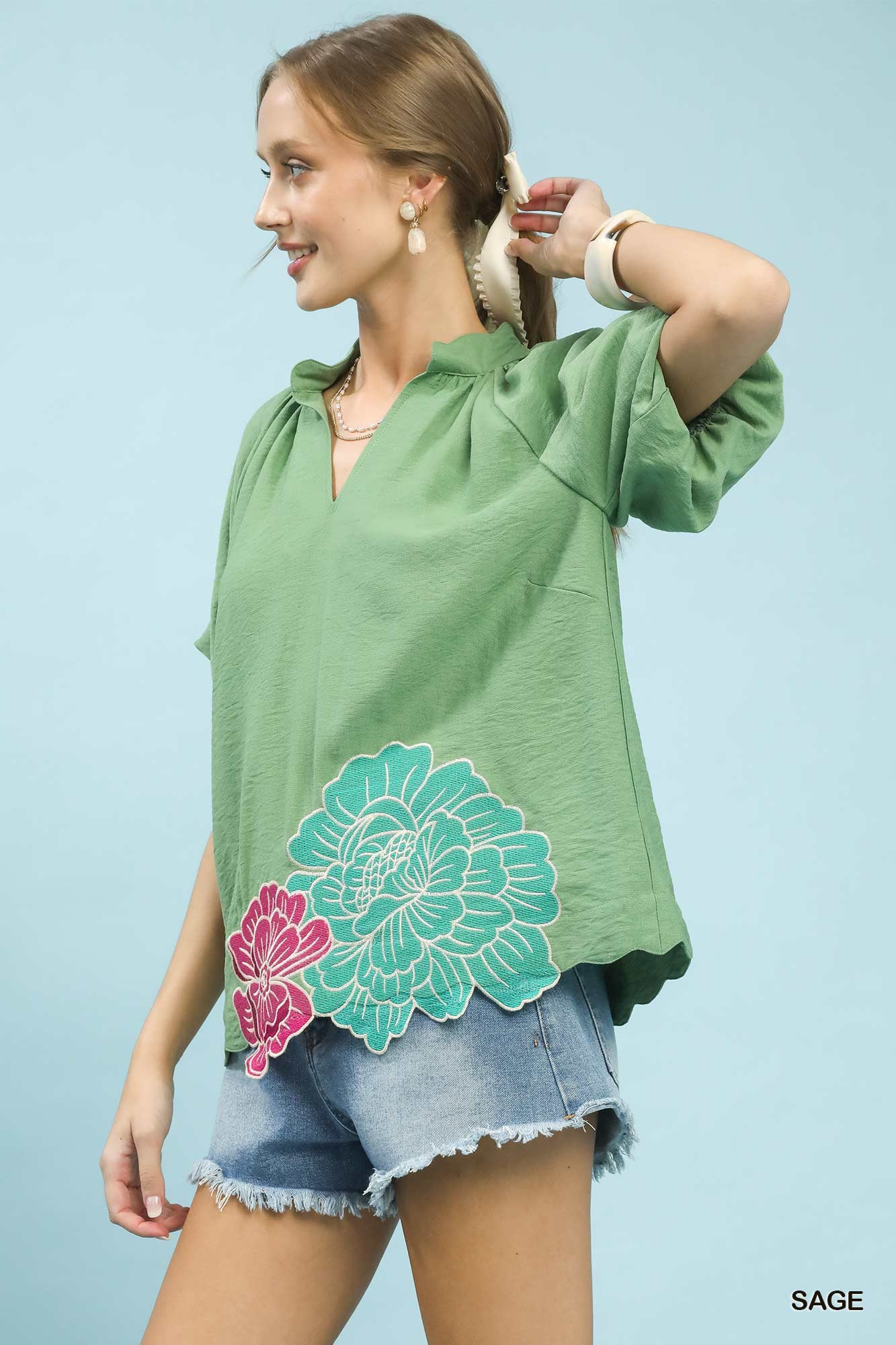 Woman wearing a green top with floral designs on a light blue background