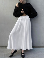 Person wearing a black cropped sweater and white skirt against a gray wall.