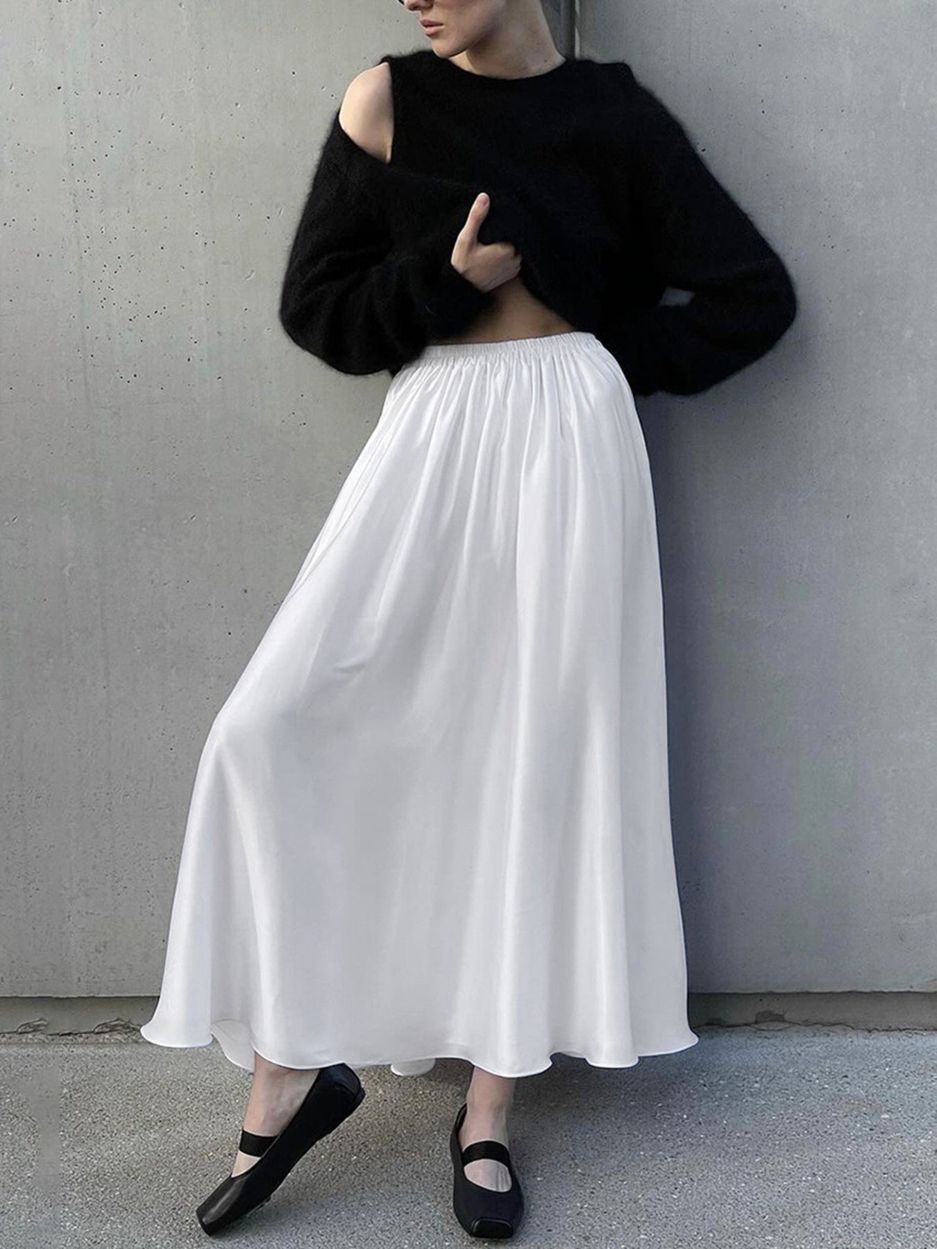 Person wearing a black cropped sweater and white skirt against a gray wall.