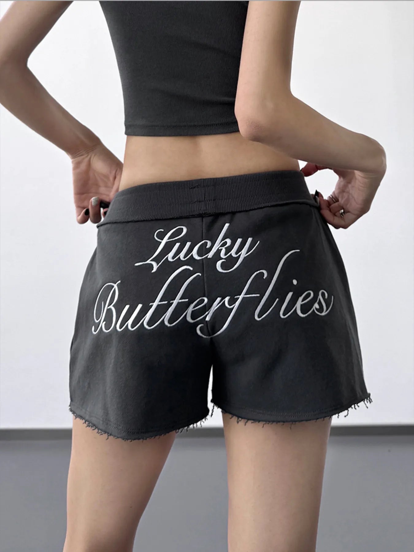 Black shorts with 'Lucky Butterflies' text worn by a person on a plain background