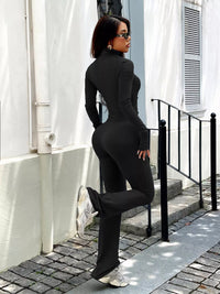 Woman in a black outfit standing on a street with white walls and a black railing.