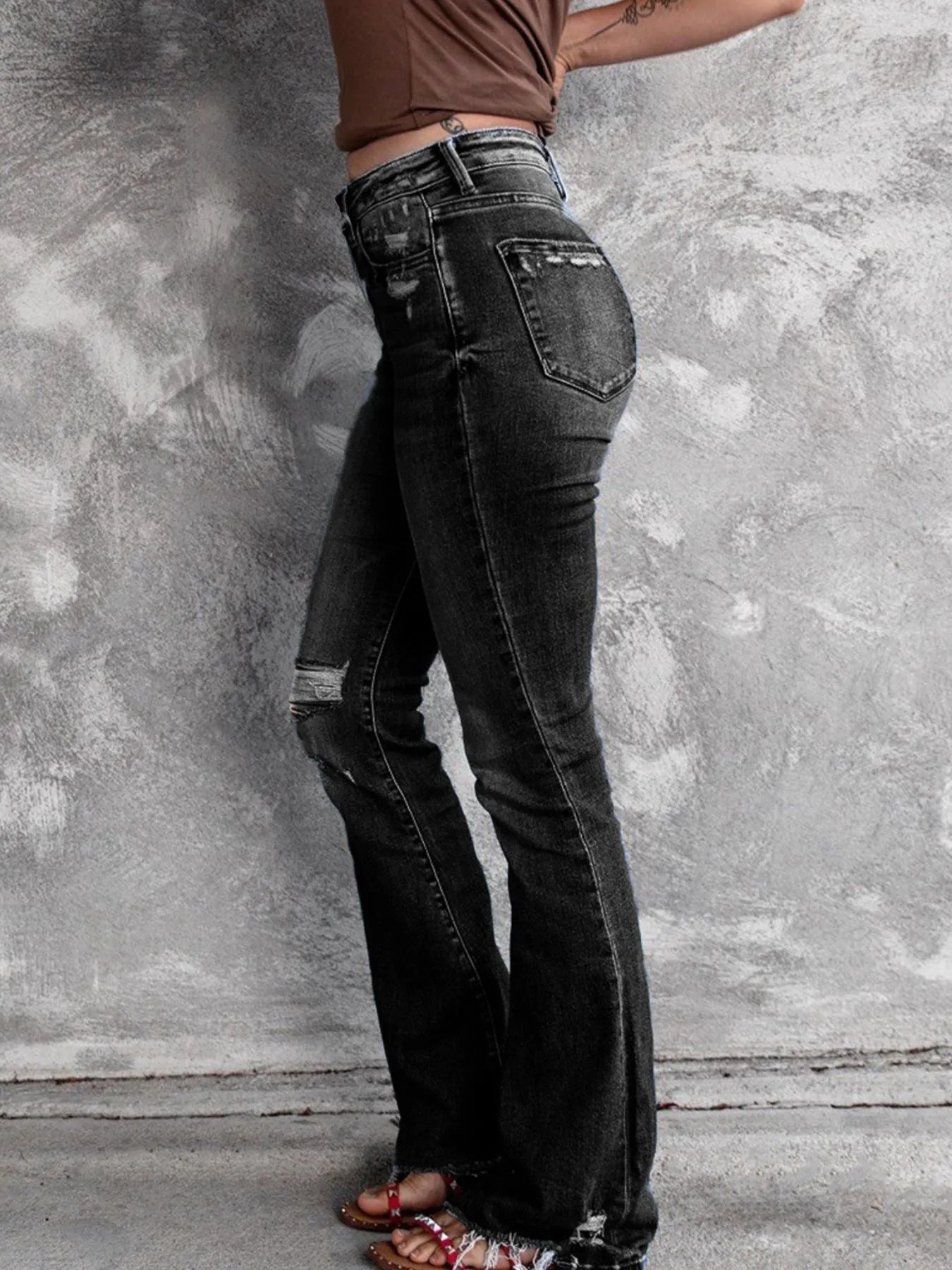 Person wearing black flared jeans against a textured gray wall.
