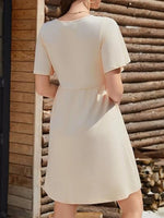 Woman wearing a beige dress standing against a wooden wall.