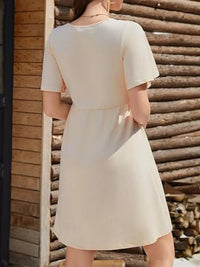Woman wearing a beige dress standing against a wooden wall.