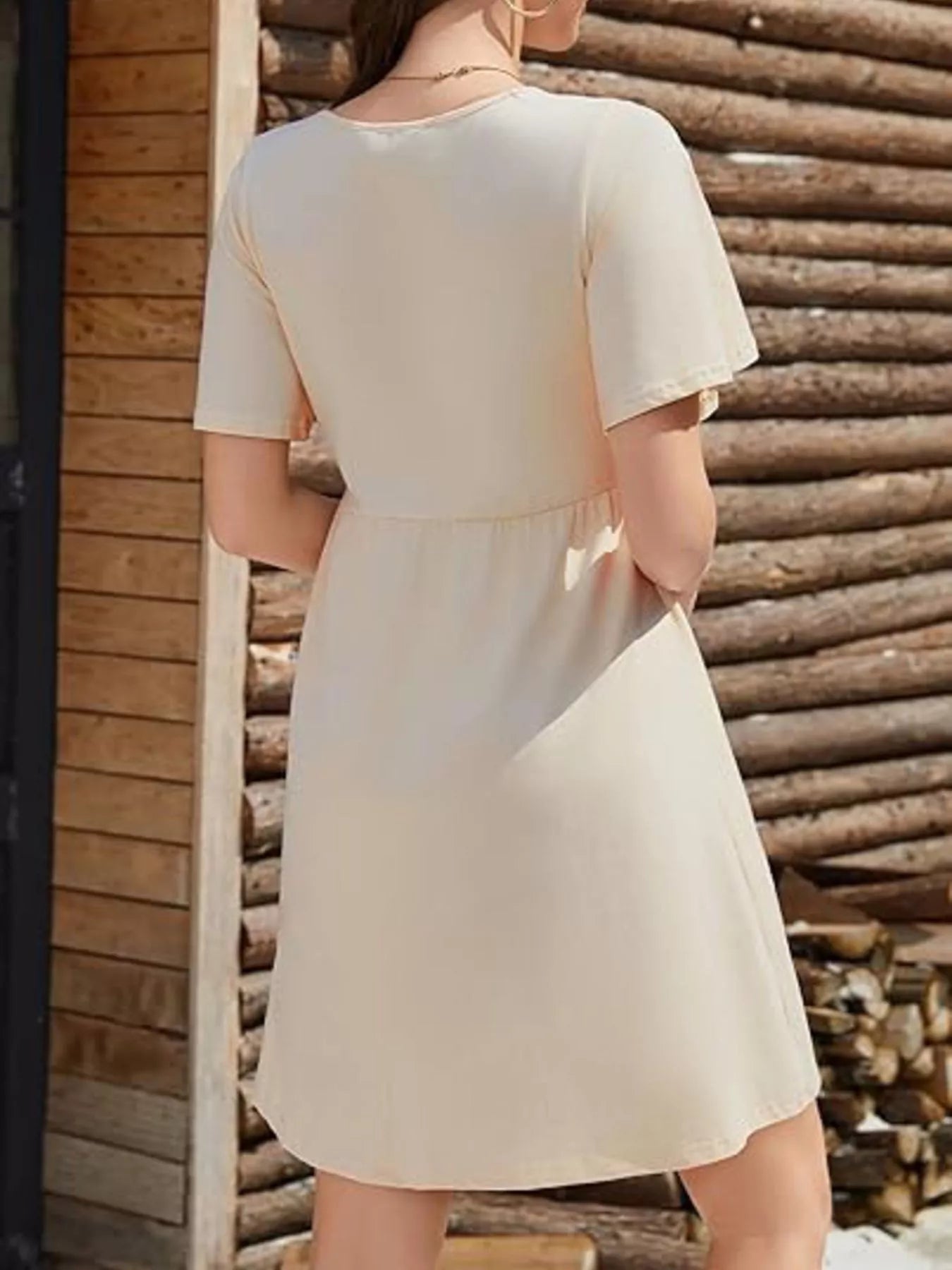 Woman wearing a beige dress standing against a wooden wall.
