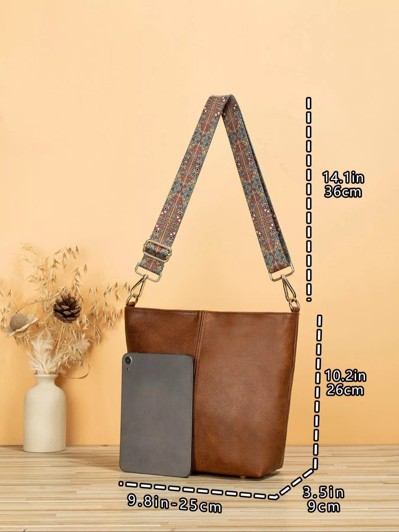 Brown leather handbag with a patterned strap on a wooden surface and beige background