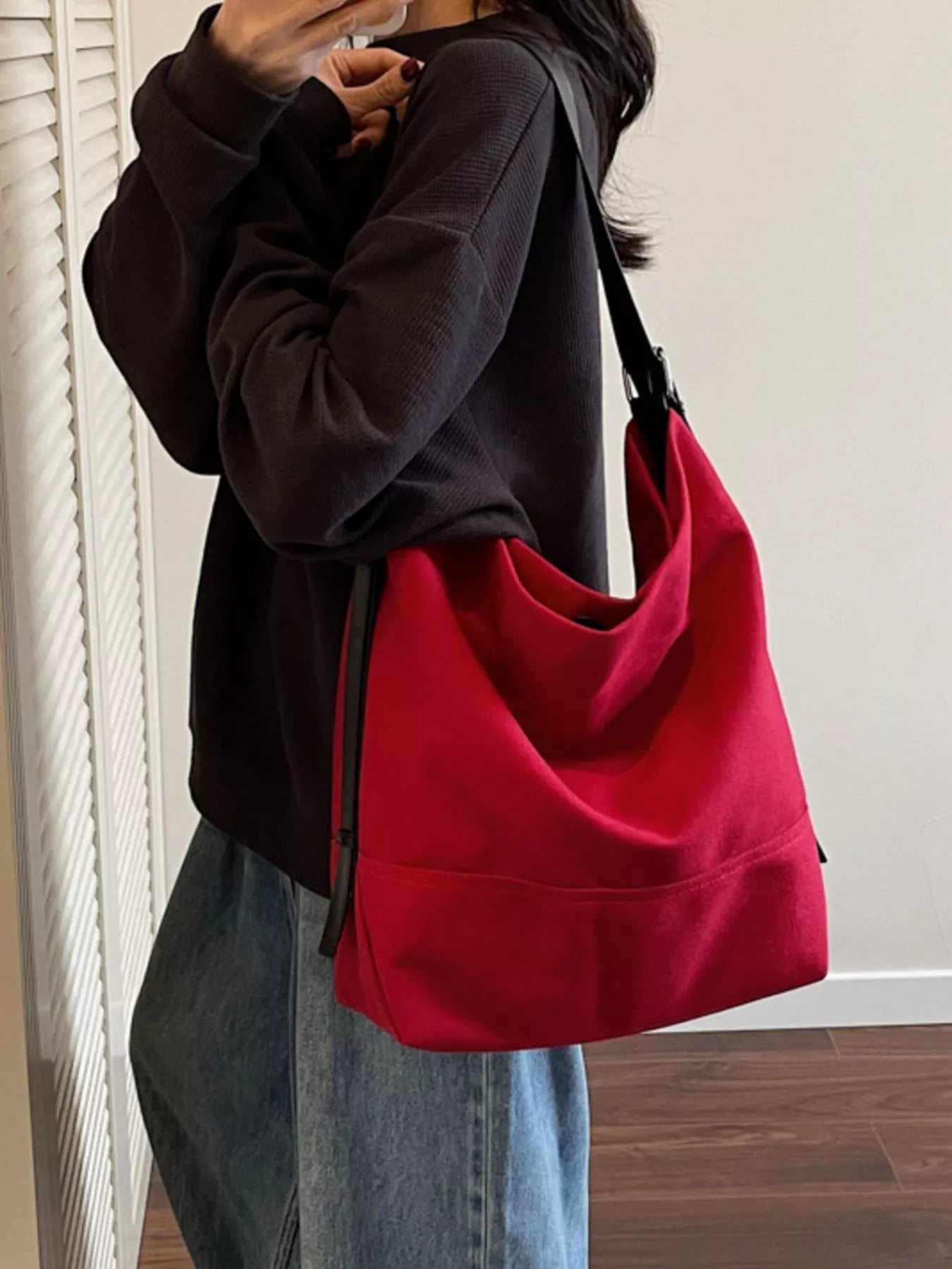 Person wearing a black hoodie and blue jeans with a red bag over one shoulder.