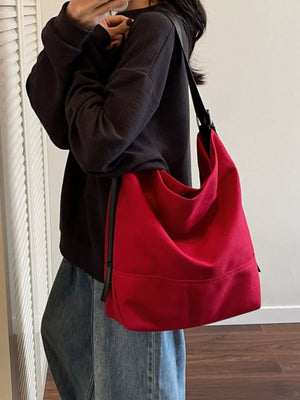 Person wearing a black hoodie and blue jeans with a red bag over one shoulder.