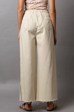 Person wearing beige wide-leg pants against a gray background