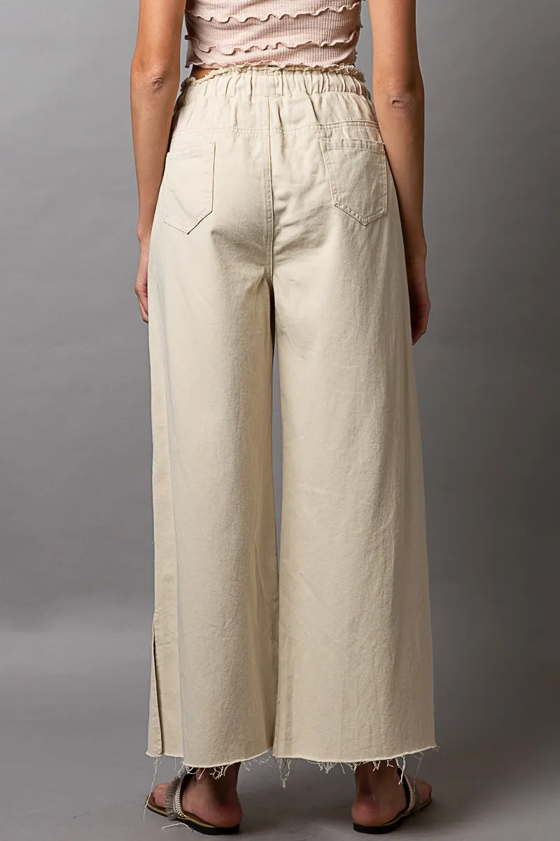Person wearing beige wide-leg pants against a gray background