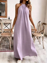 Woman wearing a long lilac dress in a room with wooden chairs and a mirror.