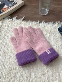 Pair of pink gloves with purple cuffs on a textured surface.