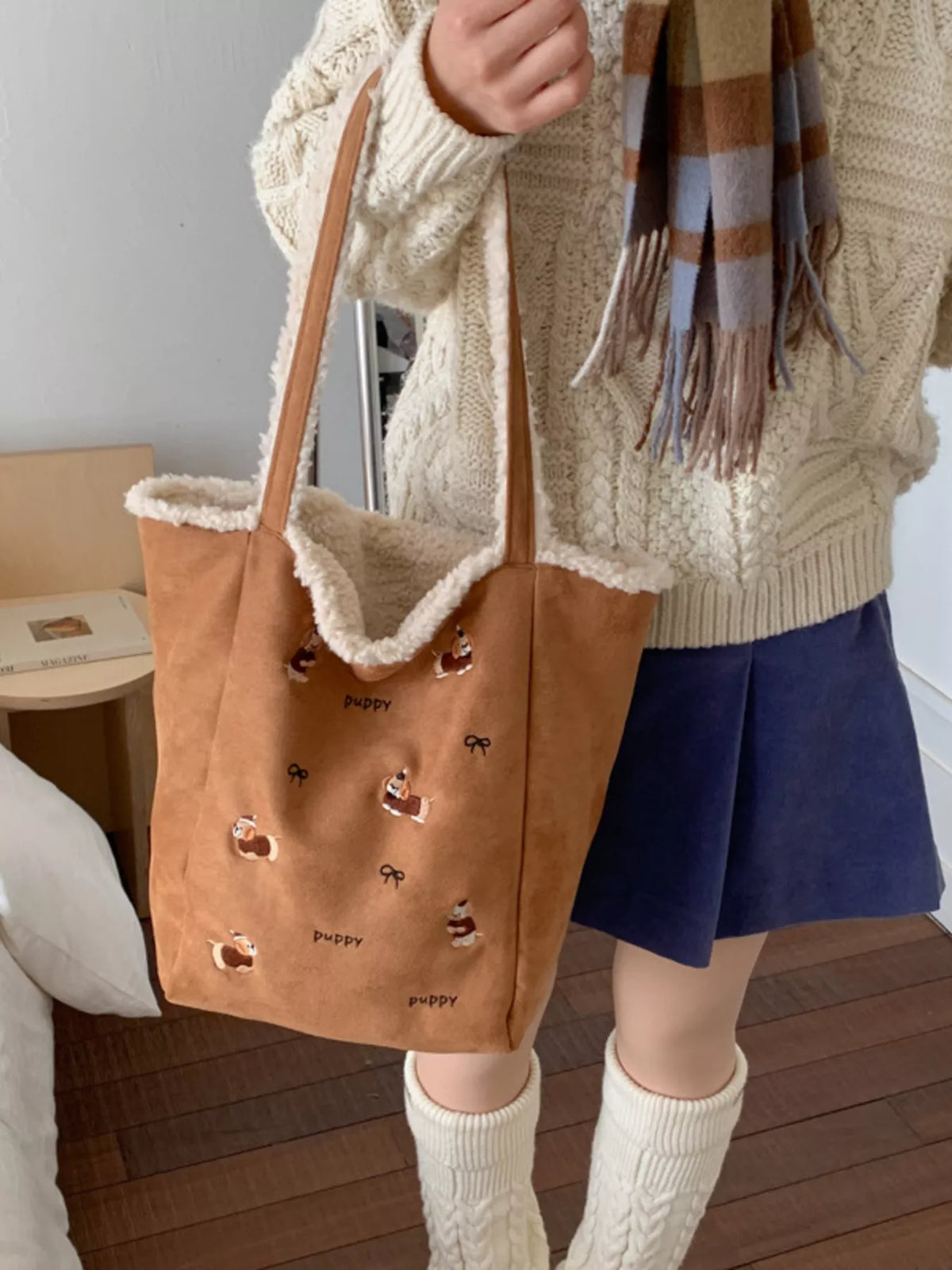 Person holding a brown tote bag with dog designs, wearing a beige sweater and blue shorts.