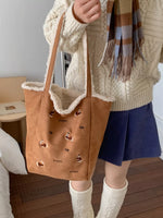 Person holding a brown tote bag with dog designs, wearing a beige sweater and blue shorts.