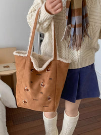 Person holding a brown tote bag with dog designs, wearing a beige sweater and blue shorts.